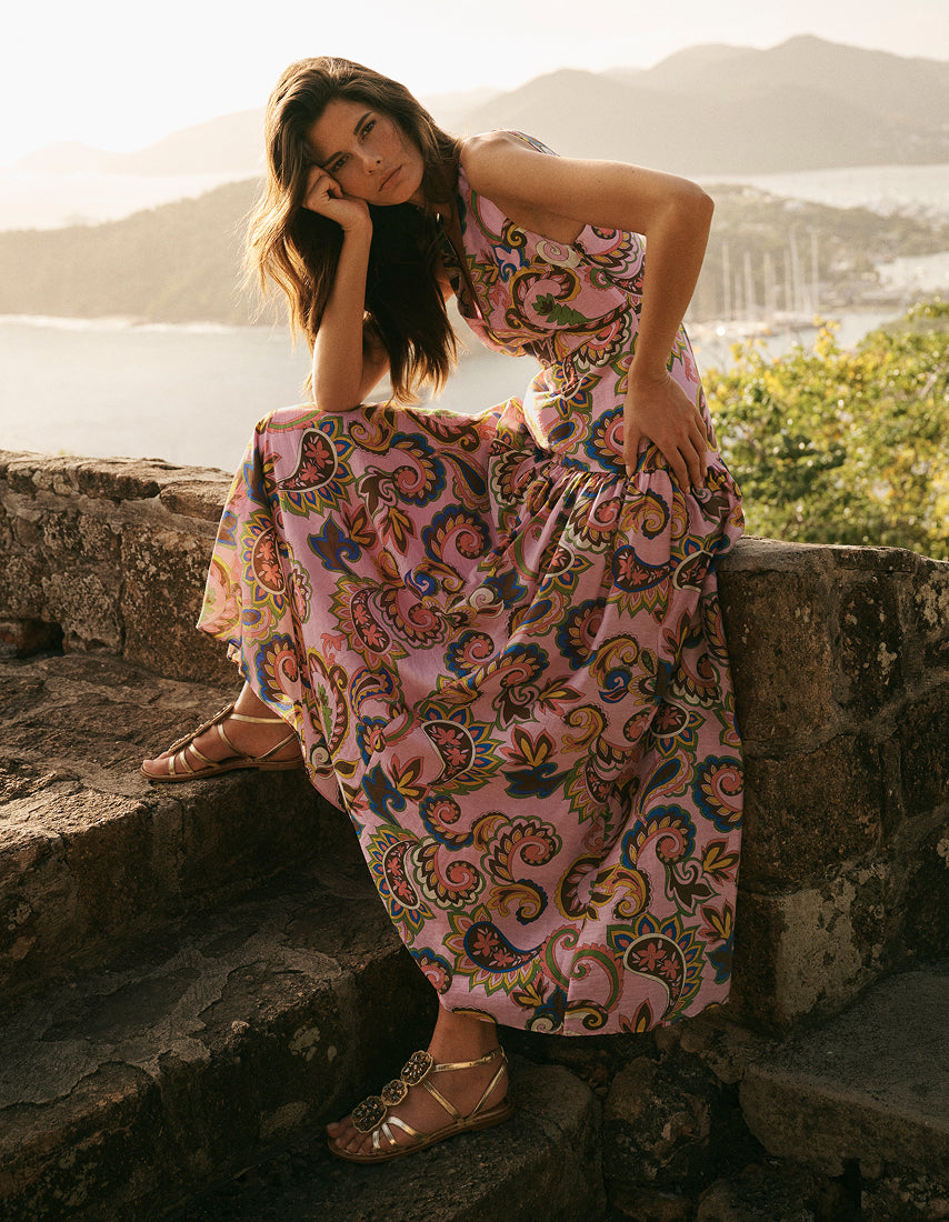 Woman in a patterned dress sitting on stone steps with a scenic background