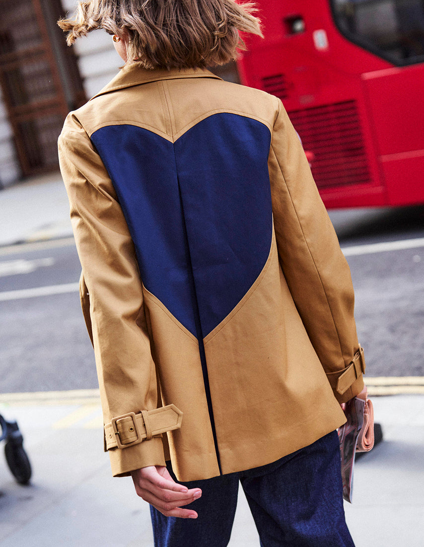 Person wearing a tan coat with a blue heart design on a street.