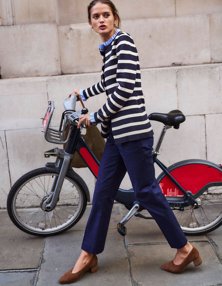 Woman in a striped sweater and blue pants walking past a bicycle on a city street.