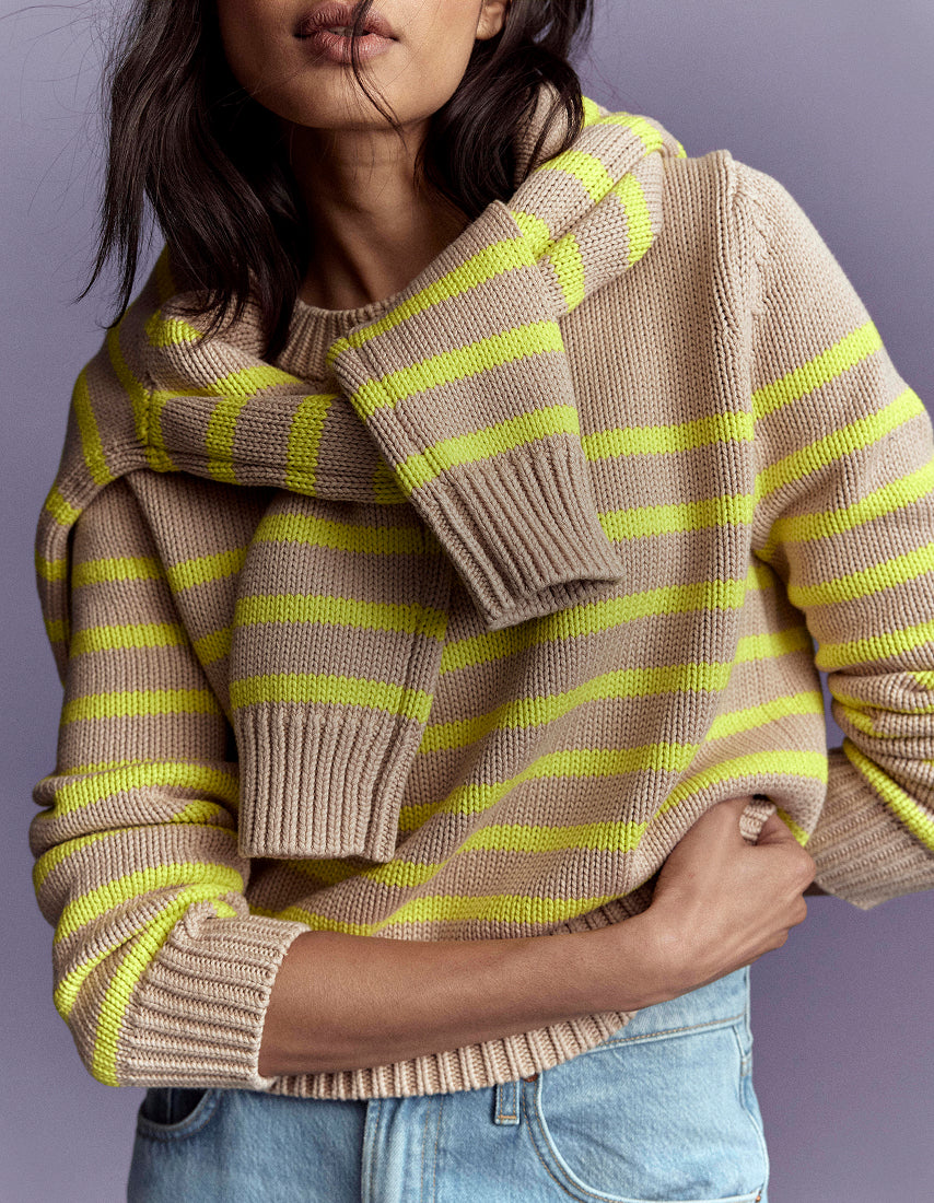 Person wearing a beige and green striped sweater with a plain background