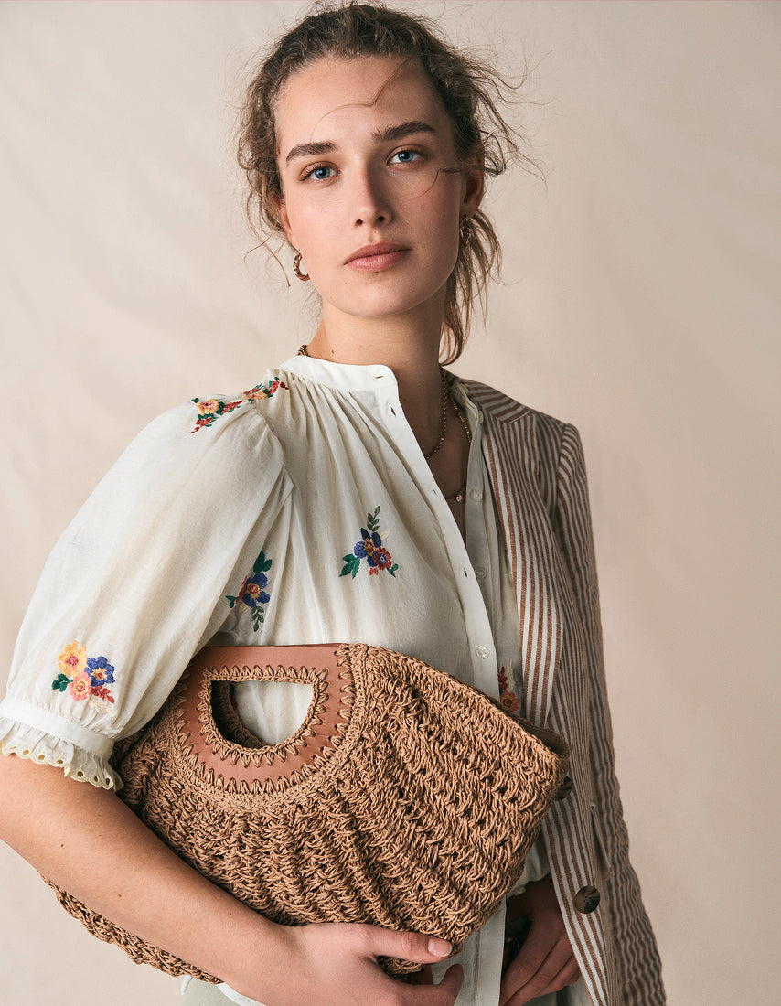 Woman holding a woven bag against a plain background
