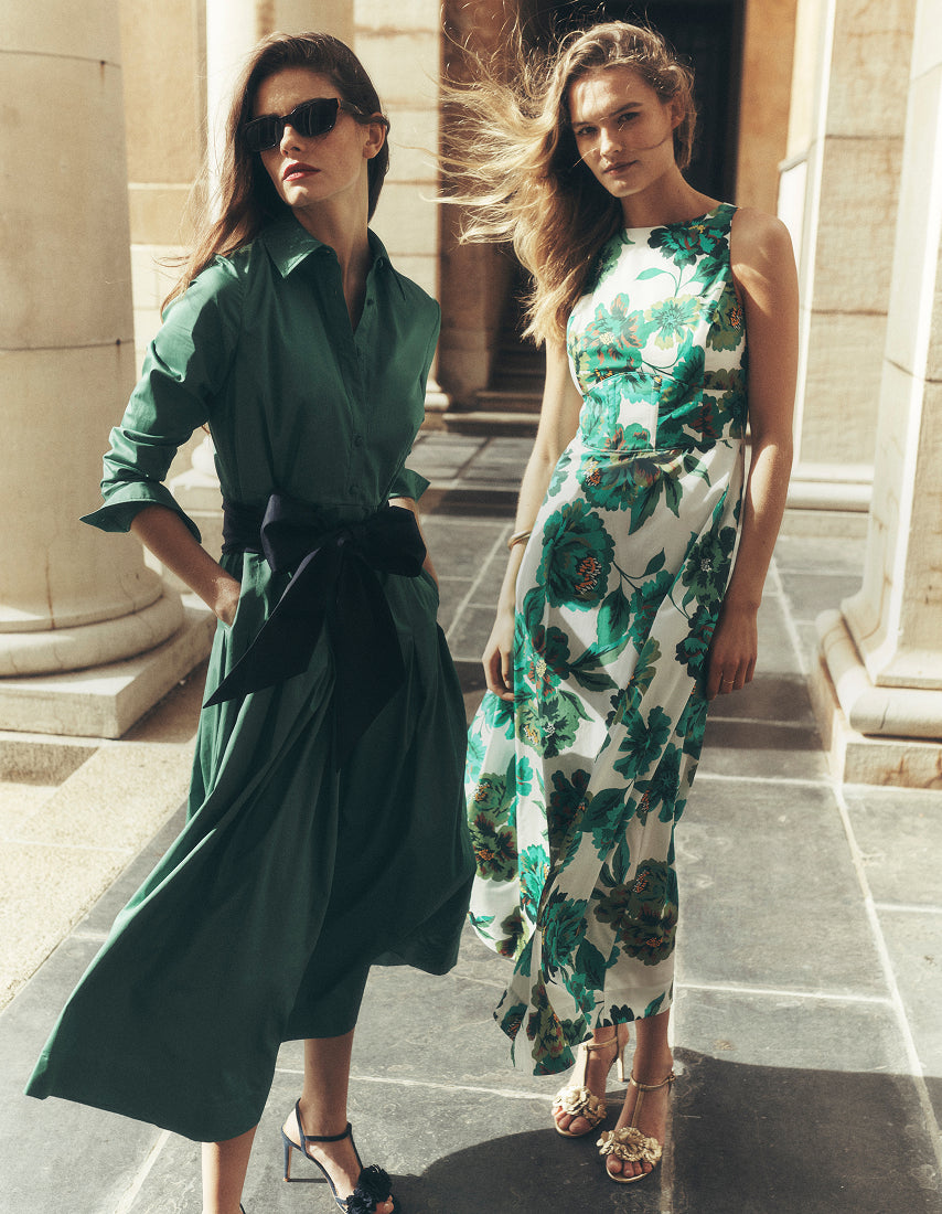 Two women in green outfits standing outdoors with classical architecture in the background