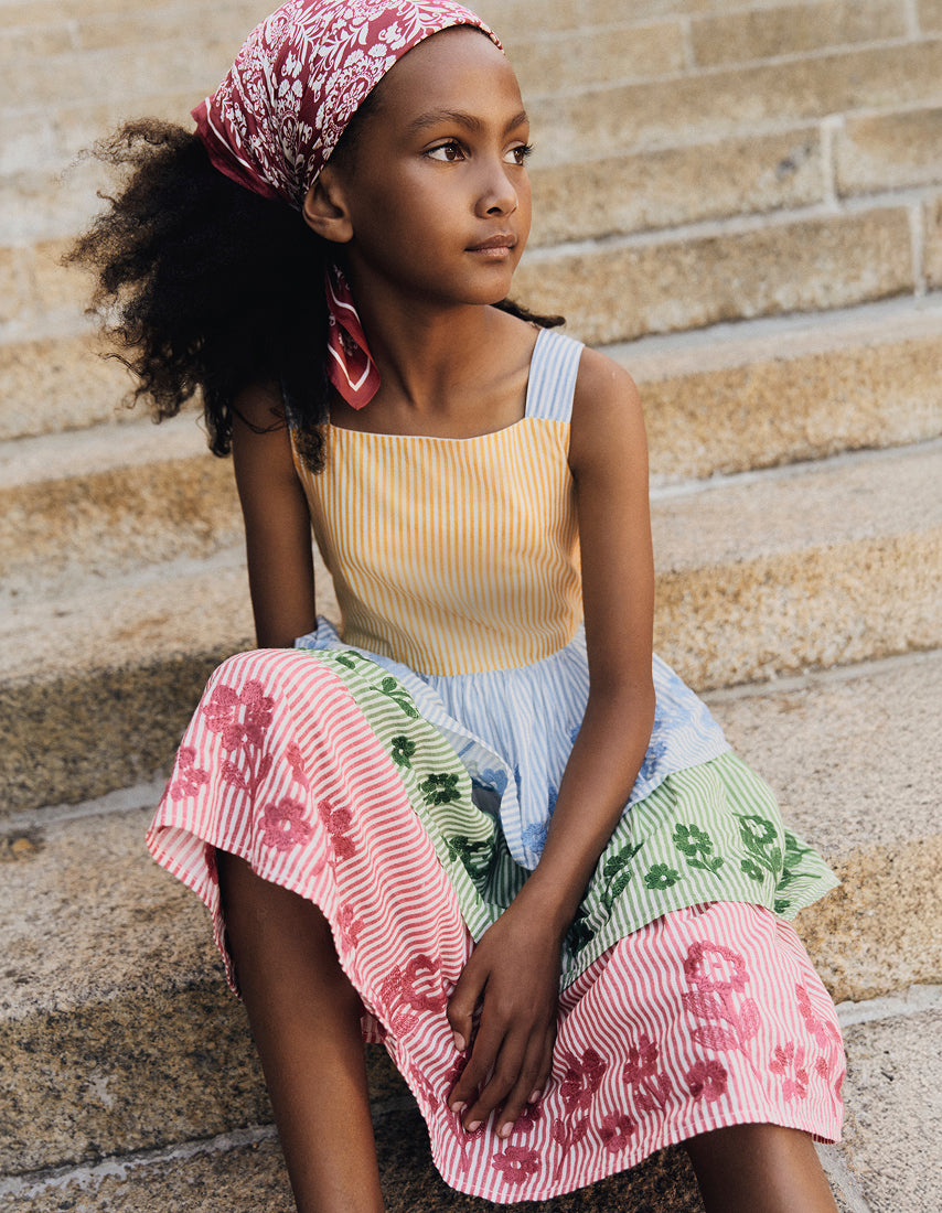 Young girl sitting on steps wearing a colorful dress and headscarf.