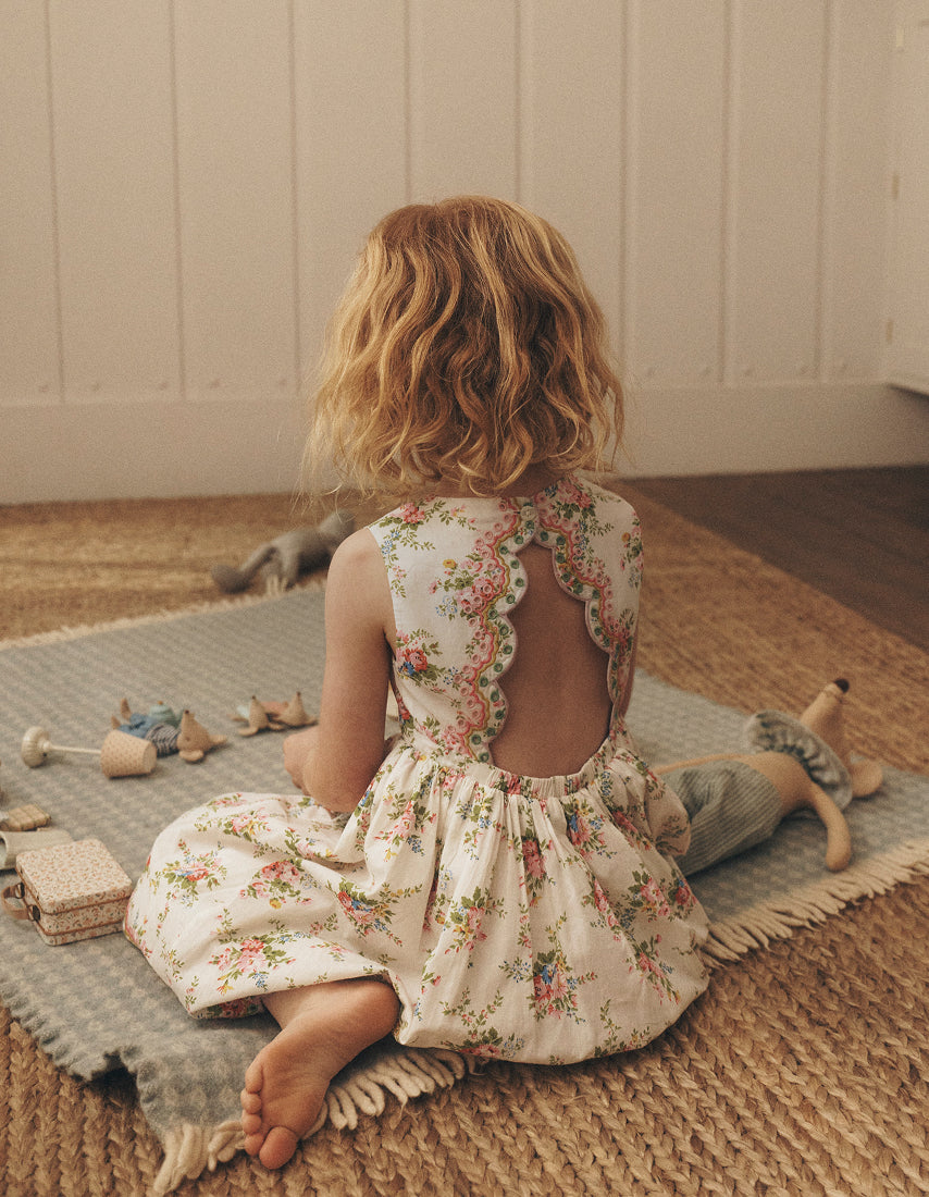 Child in a floral dress sitting on a rug with toys around