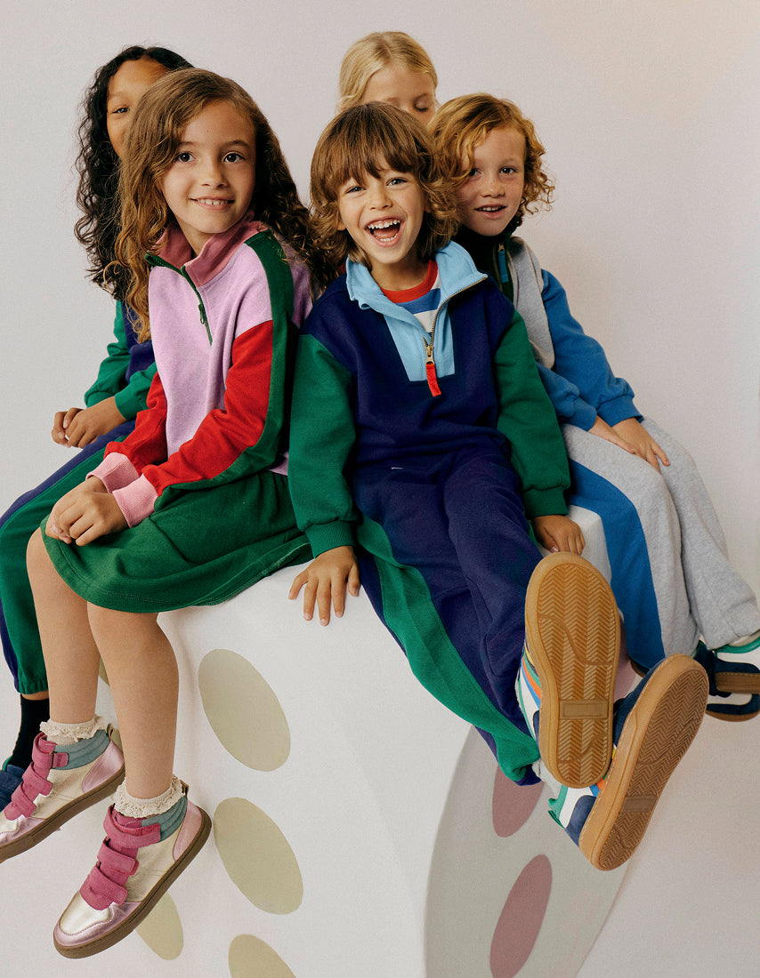 Children sitting on a polka dot chair wearing colourful outfits.
