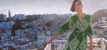 Woman in a green dress standing on a balcony with a cityscape in the background