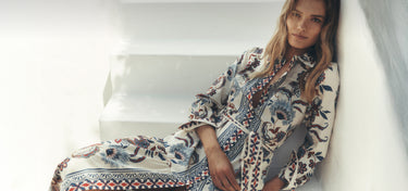 Woman wearing a patterned dress sitting on a white couch.