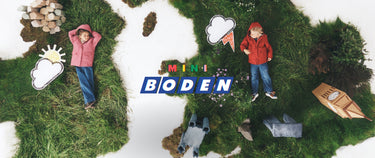 A children's play set or miniature scene featuring two children lying on grassy terrain with toy clouds, a small boat, and the central text 'MINI BODEN'.