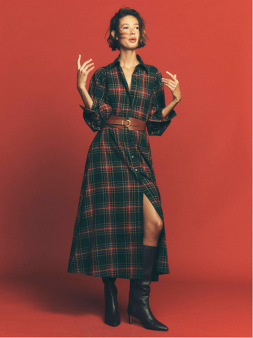 Woman in red tartan shirt dress standing in front of a red background.