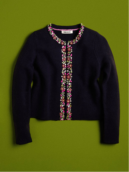 A dark navy knit cardigan sweater with colorful floral embroidery down the front and around the collar, displayed flat against a solid olive green background.