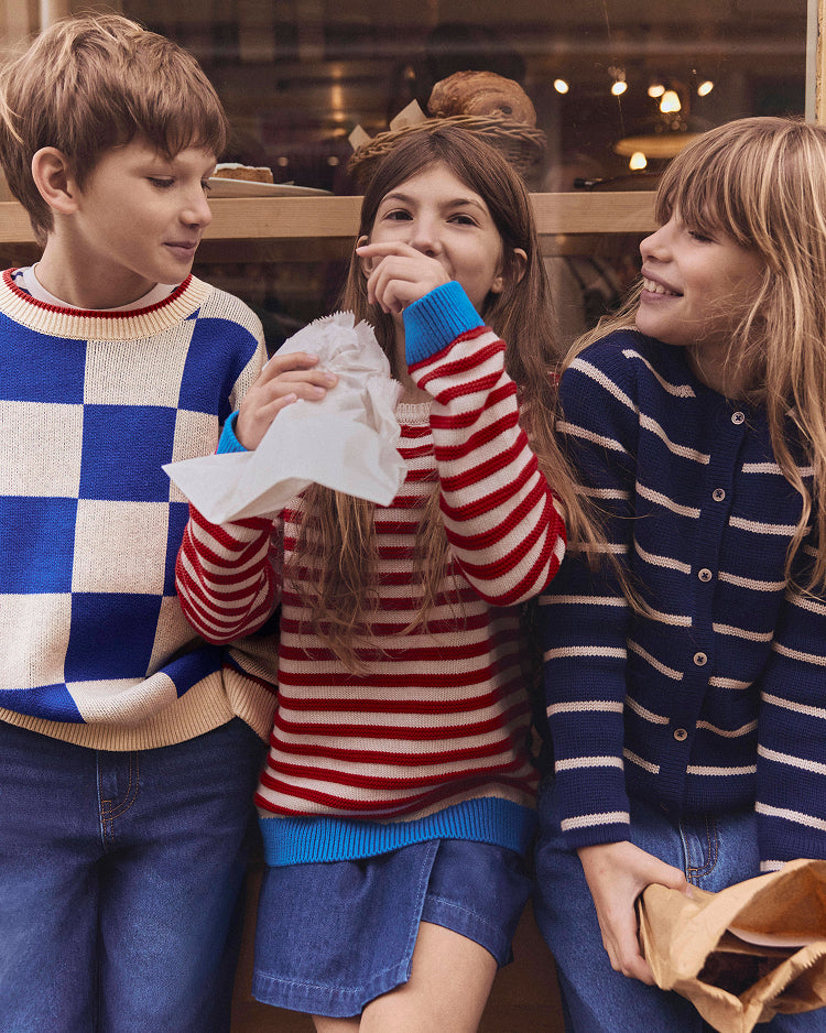 Three children wearing colorful sweaters standing together indoors.