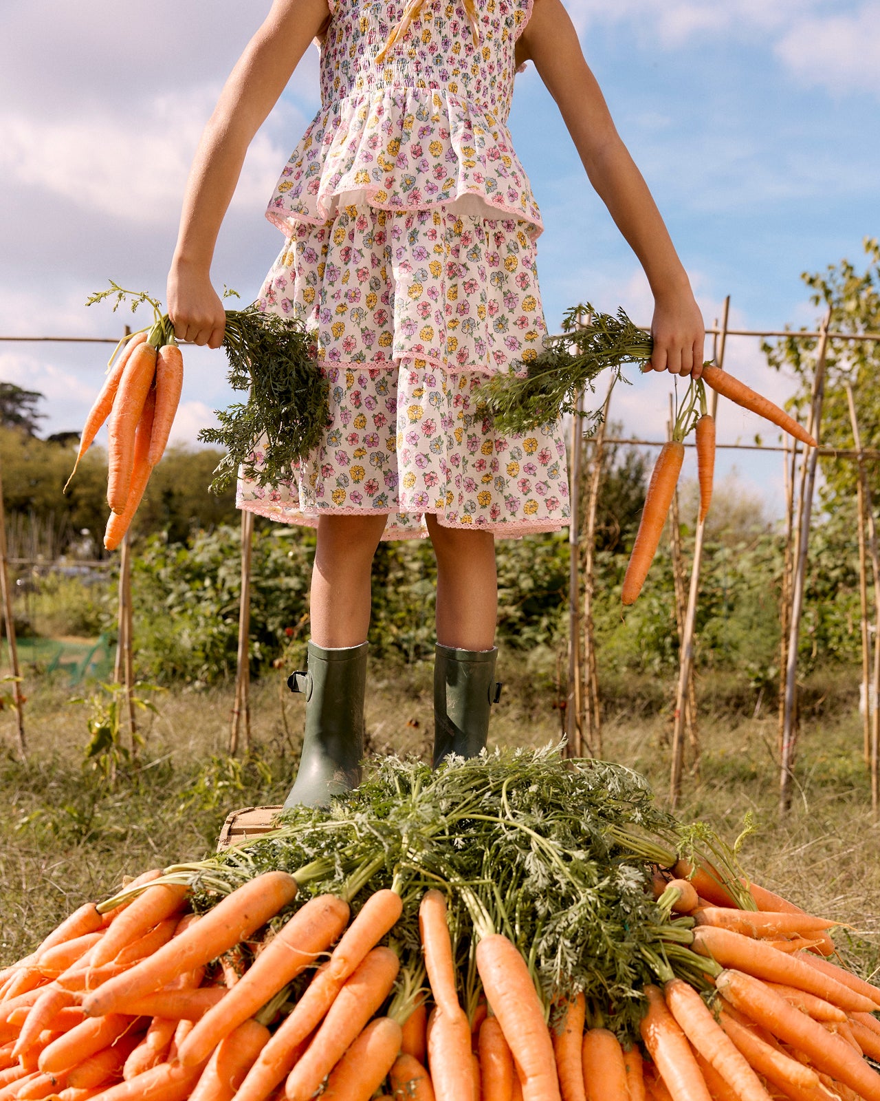 Person in a garden holding carrots with a pile of carrots in front