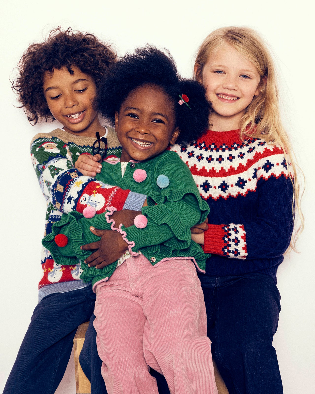 Three children wearing colorful sweaters against a white background