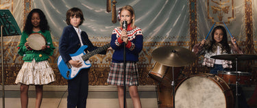 Four children playing musical instruments in a decorated room.