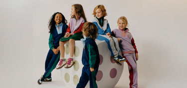 Five children in colourful outfits sitting on a polka dot chair against a white background