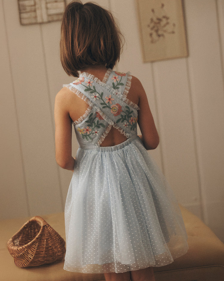 Child wearing a floral dress with a textured wall and basket in the background