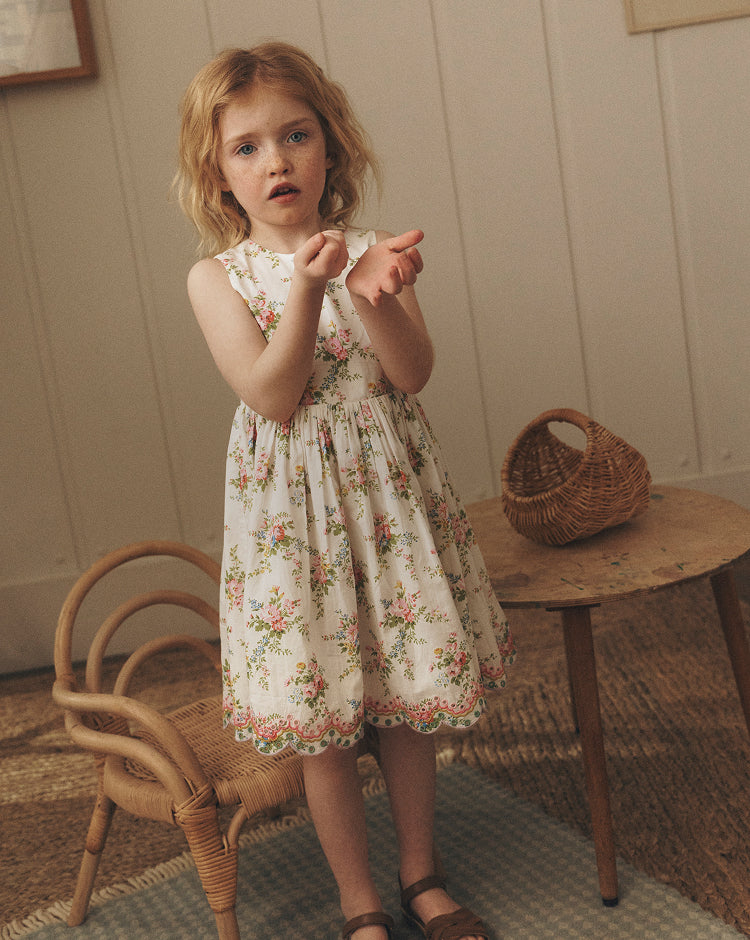 Young girl in a floral dress standing in a room with wooden furniture and a basket.