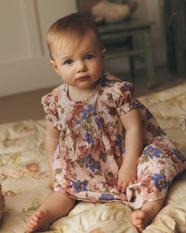 Baby in a floral dress sitting on a bed with a soft focus background