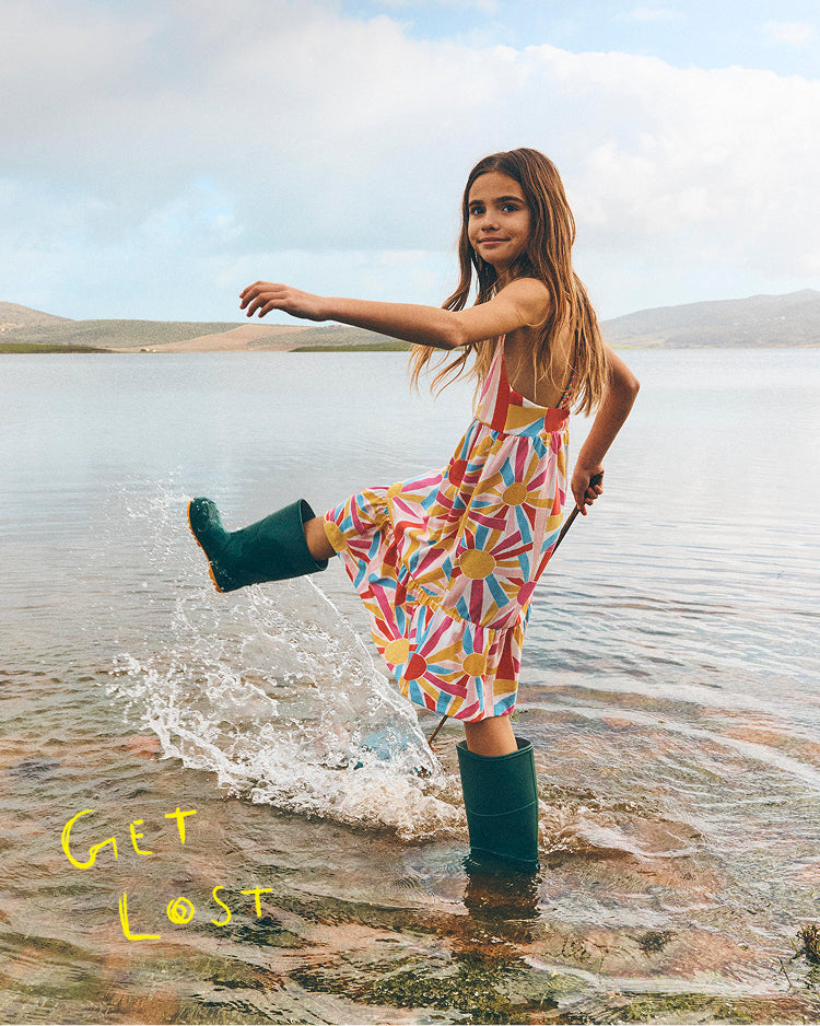 Girl in colorful dress and green rain boots playing in water with 'Get Lost' text.