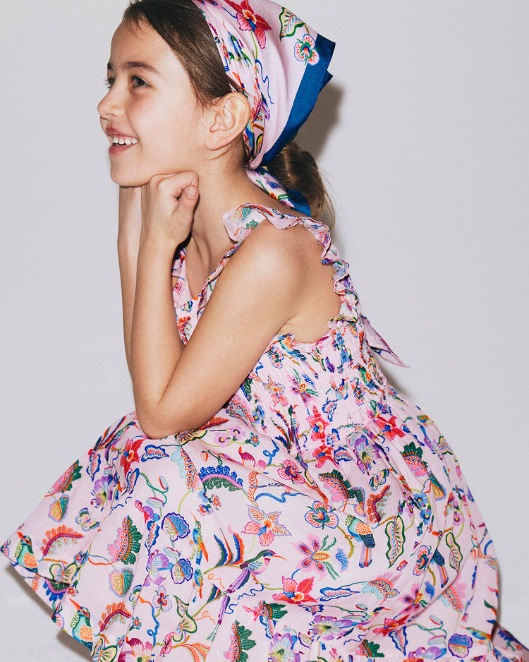 Young girl wearing a colorful floral dress and headscarf on a plain background