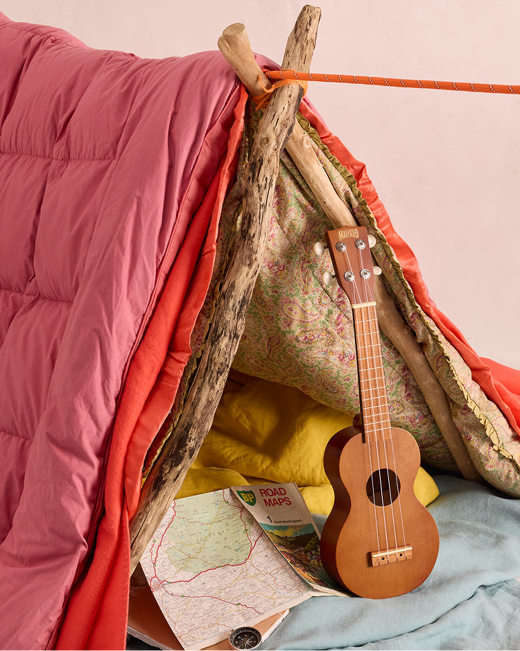 Small wooden ukulele inside a cozy, handmade playhouse with pink fabric and driftwood structure.