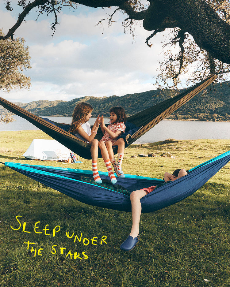Two children sitting in a hammock with a scenic background and text 'Sleep under the stars'.