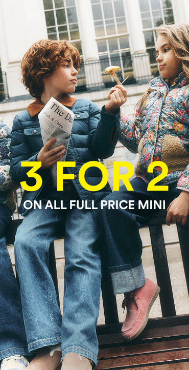 A promotional lifestyle image showing two children sitting on a bench outdoors, wearing colorful puffer jackets and jeans. Large yellow and white text overlays read '3 FOR 2 ON ALL FULL PRICE MINI'.