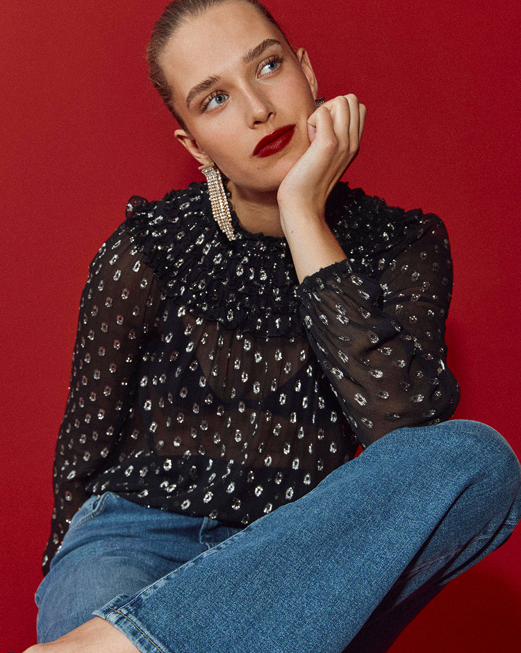 Woman wearing a black patterned blouse and blue jeans against a red background