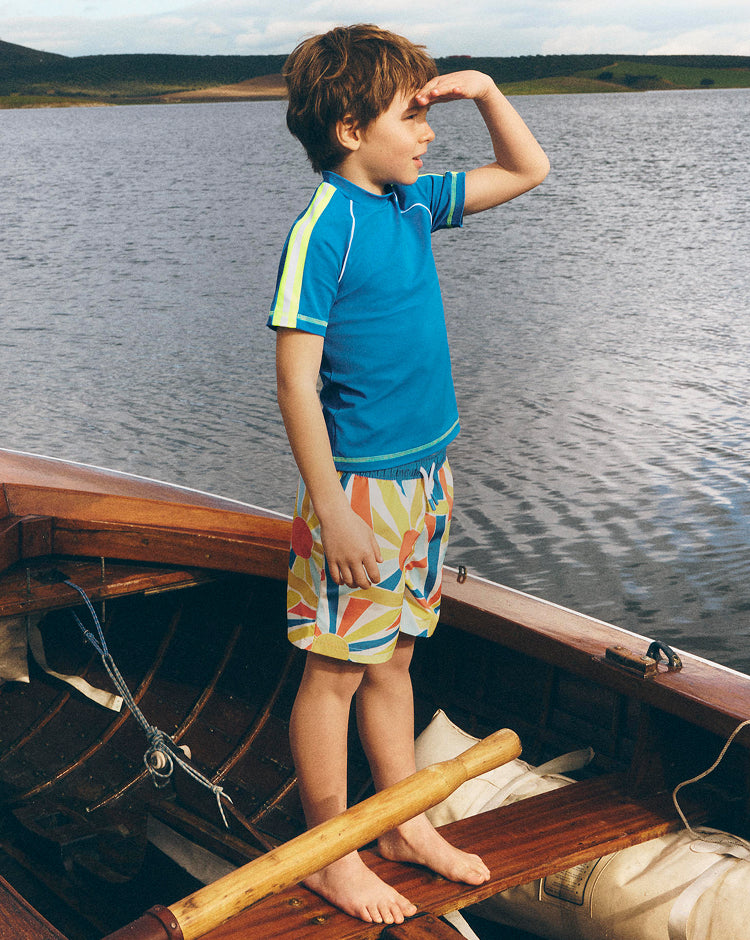 Child standing on a wooden boat by a lake