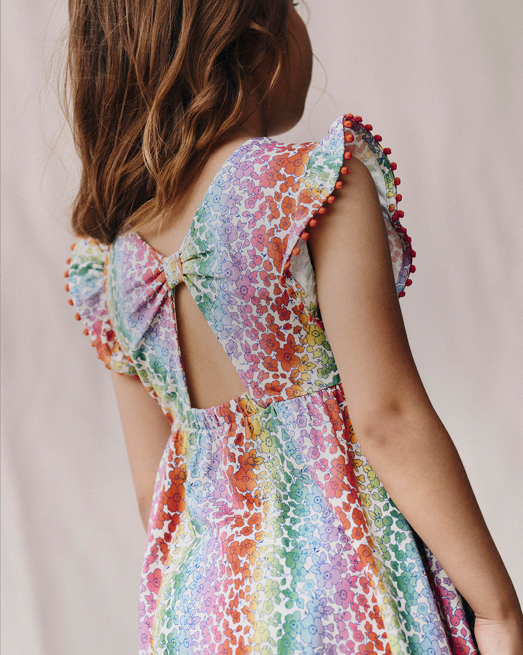 Colorful dress with floral pattern and pom-pom details on a plain background