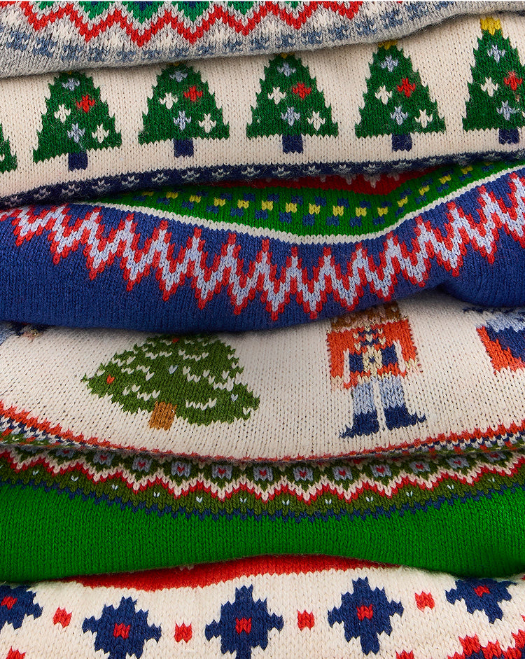 Stack of Christmas-themed sweaters with tree and snowflake patterns.