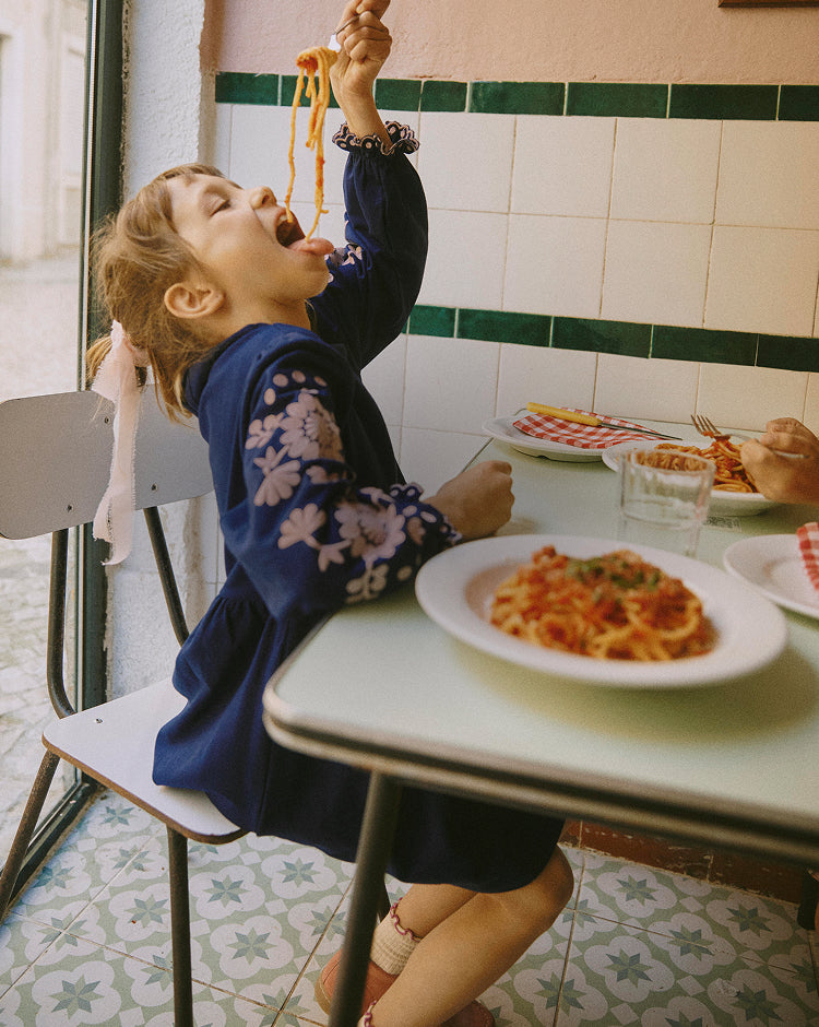 Child eating spaghetti in a restaurant with a plate of pasta on the table.