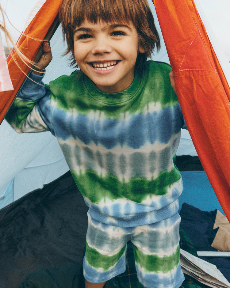 Child wearing a tie-dye outfit standing inside a tent