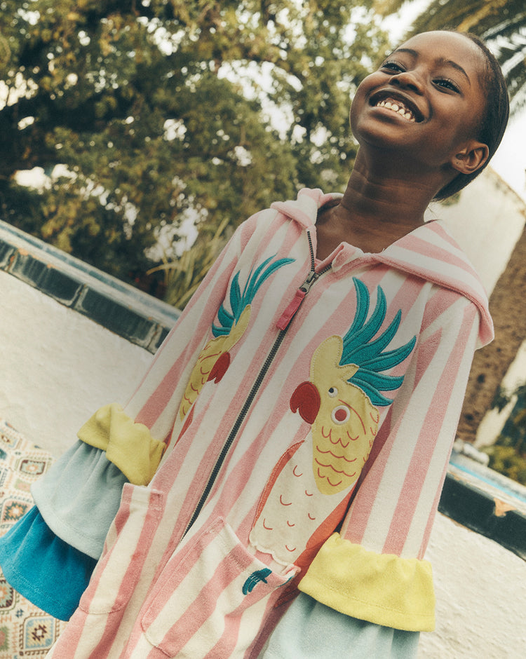 Child wearing a colorful pink jacket with a parrot design outdoors.