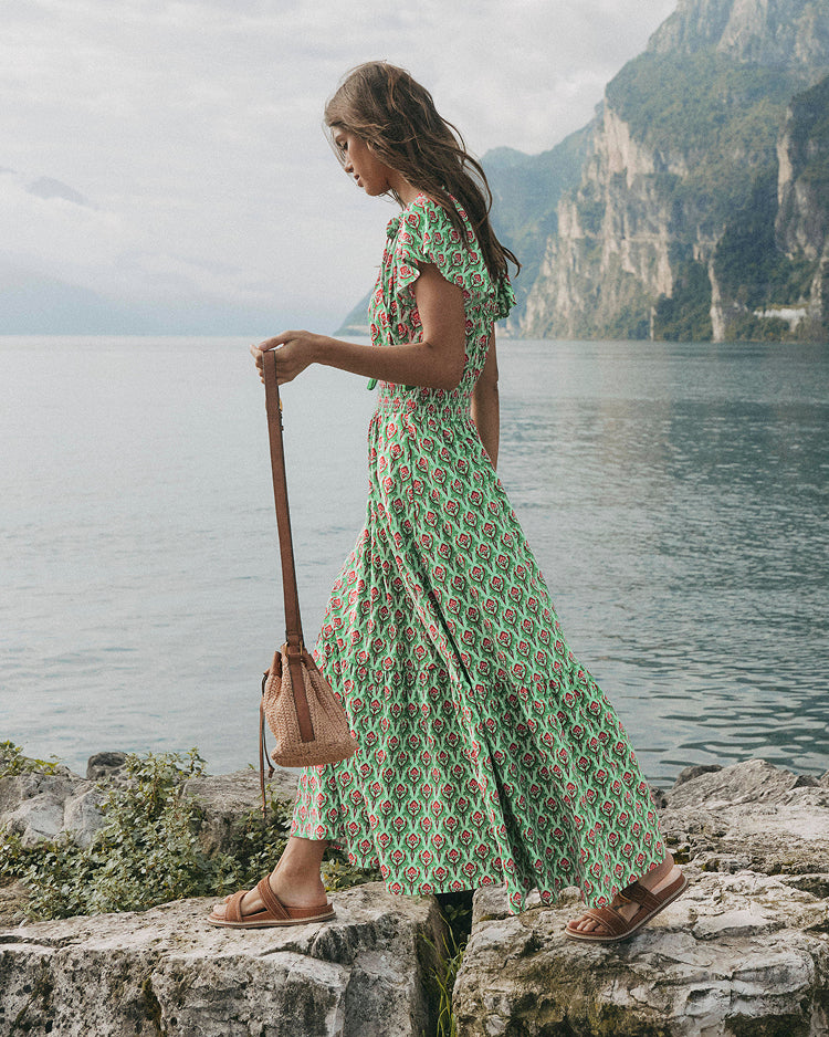 Woman in a green floral dress standing by a lake with mountains in the background