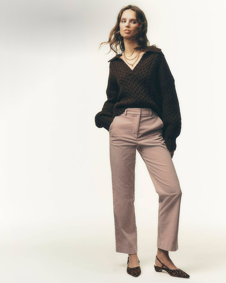 A woman modeling a dark brown textured knit sweater, light brown straight-leg trousers, and brown patterned flat shoes against a plain white studio background.