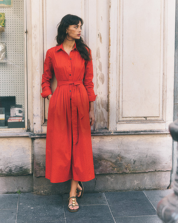 Woman wearing a red dress standing against a building wall.