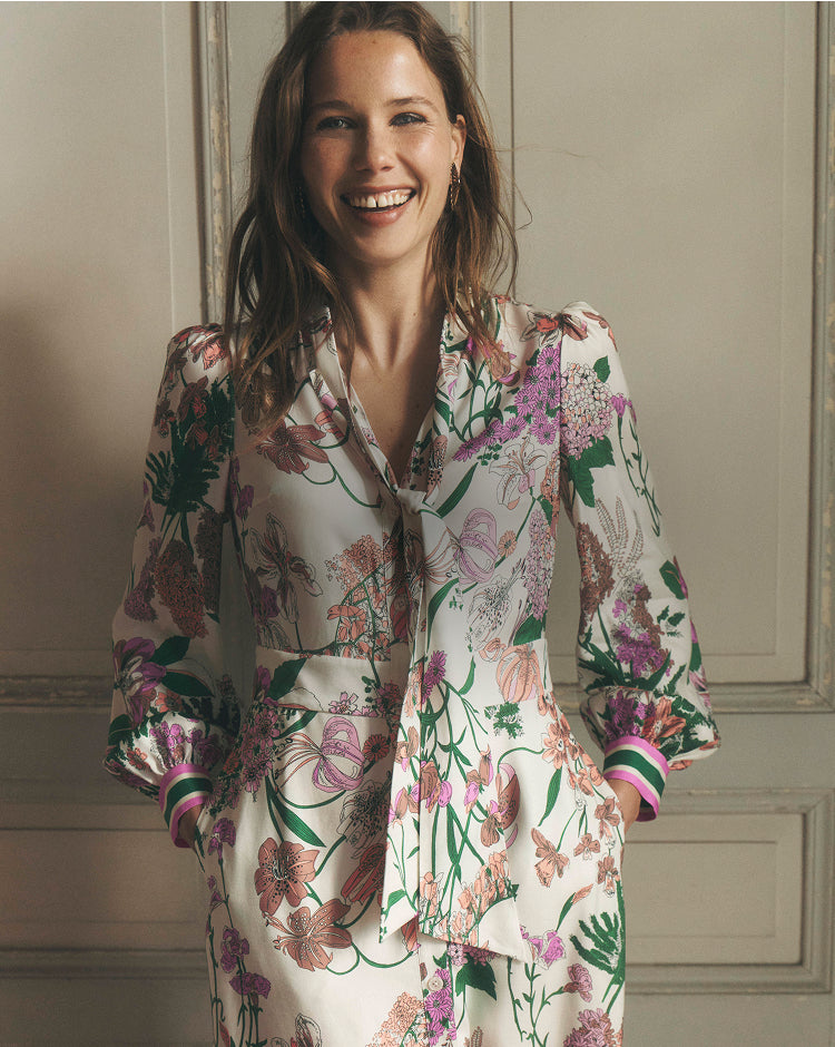 Woman wearing a floral outfit against a neutral wall.