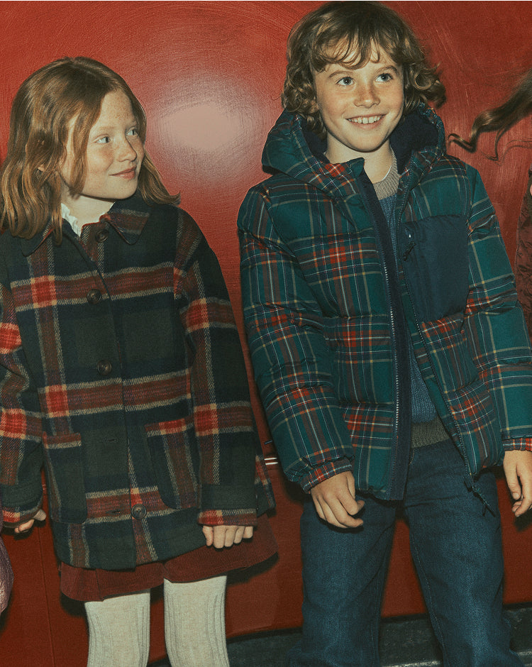 Children in Tartan jackets standing against a red wall