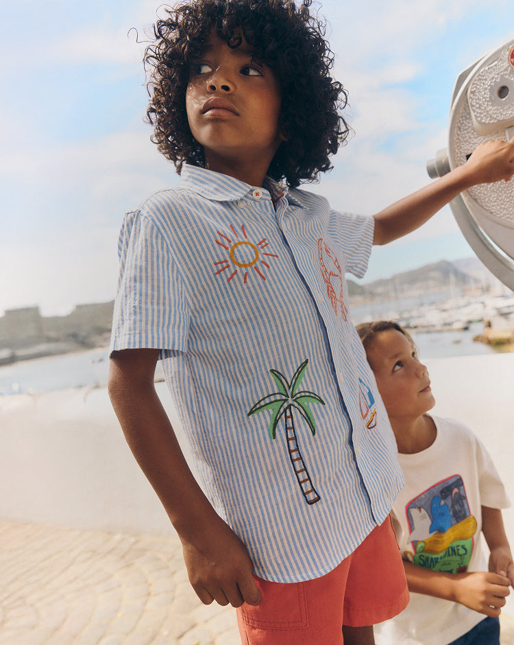 Child wearing a shirt with a palm tree design by a waterfront