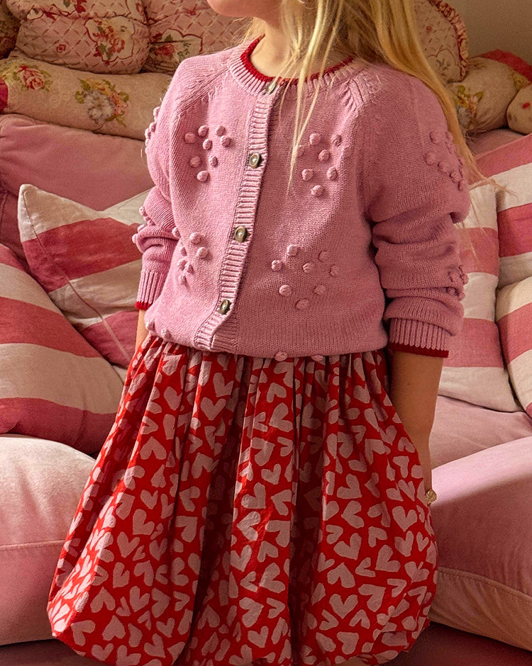 Child wearing a pink cardigan with button details in a cozy indoor setting.
