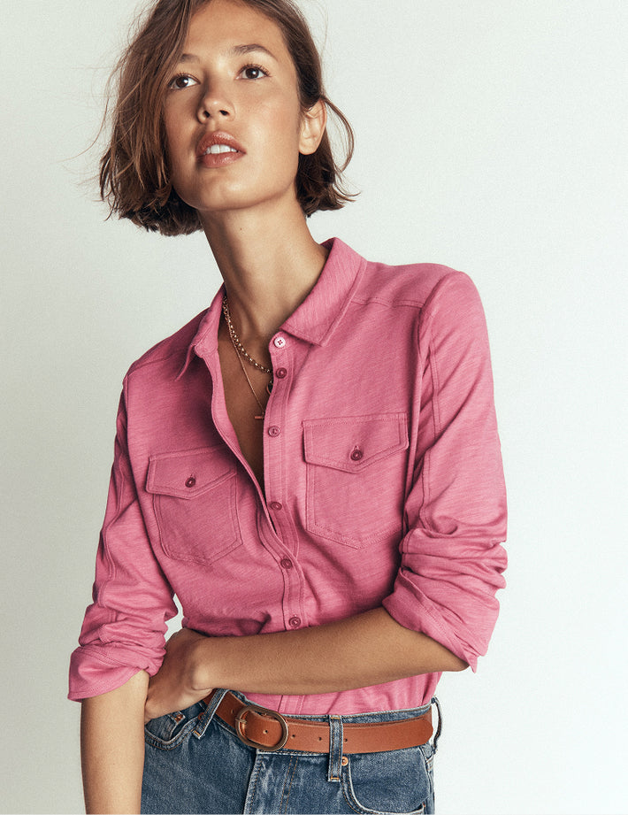 Woman wearing a pink shirt and jeans against a plain background