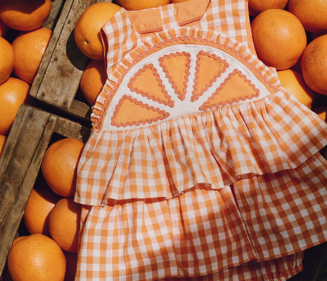 Children's dress with orange and white checkered pattern among oranges