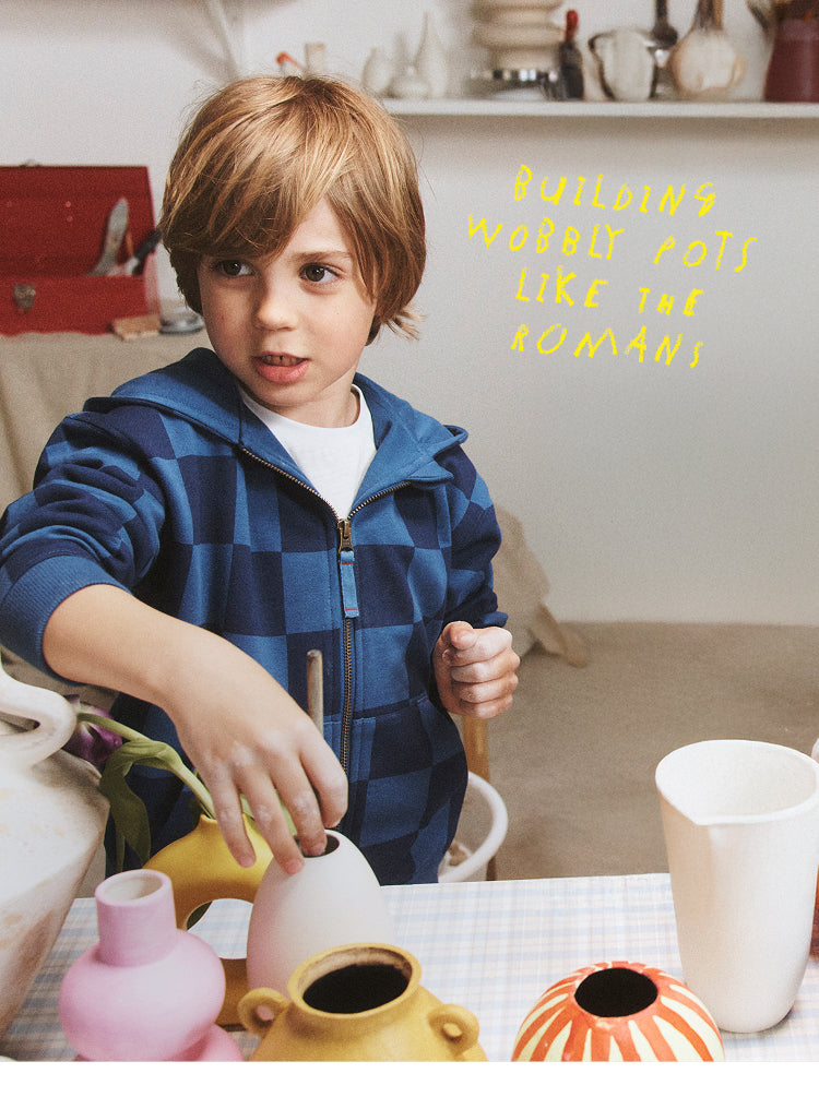 Child working with pottery at a table, with text 'Building pottery pots like the Romans' on a shelf.