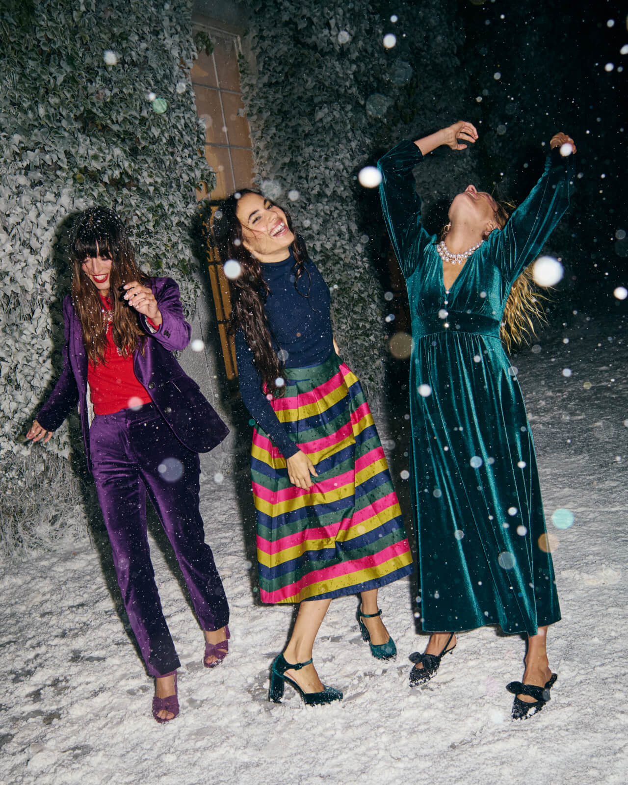Three women in colourful outfits dancing in the snow.