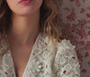 Close-up of a person wearing a white lace garment with a floral-patterned background